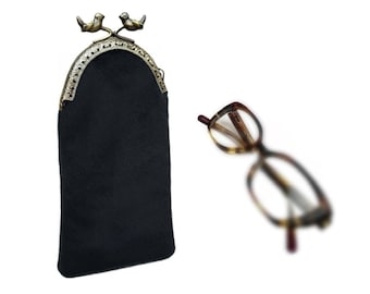 May include: A black eyeglass case with a decorative bronze-colored clasp featuring two small bird figures. The case is next to a pair of eyeglasses with a tortoiseshell pattern.