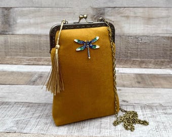 Könnte beinhalten: Senffarbene Samt-Clutch mit einer Libellenbrosche. Der Verschluss und die Kette sind bronzefarben. Eine goldene Quaste hängt am Verschluss. Die Clutch ist rechteckig und hat eine Vintage-Ästhetik.