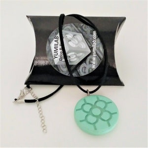 Può includere: Una collana con un ciondolo blu turchese con un design geometrico. La collana è su un cordoncino nero e viene fornita in una busta nera con il testo "YUMILAB Deco & Design www.yumilab.com".