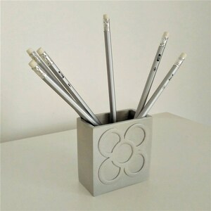 Peut inclure: Un porte-crayons en argent avec un motif de fleur. Six crayons argentés sont dans le porte-crayons.