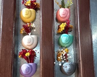 May include: A set of six seashell-shaped planters with various coloured glazes. Each planter is filled with a small bouquet of dried flowers. The planters are arranged in two rows of three on a wooden surface.
