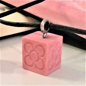 Op de afbeelding: Een roze kubus hanger ketting met een zilveren ketting. De kubus heeft een reliëf ontwerp van vier cirkels in het midden.