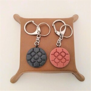 May include: Two keychains with round, decorative charms. One charm is black with a geometric design, and the other is red with the same design.