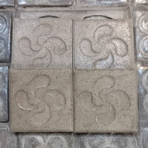 Può includere: Quattro piastrelle quadrate con un designo a stella a cinque punte in rilievo grigio. Le piastrelle sono realizzate in un materiale ruvido e testurizzato.