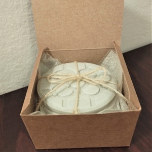 Può includere: Un sottobicchiere in cemento grigio con un design geometrico è confezionato in una scatola di cartone marrone con un rivestimento in plastica trasparente. Il sottobicchiere è legato con uno spago.