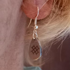 Può includere: Orecchini a goccia d'argento con un design geometrico. Gli orecchini pendono dall'orecchio di una persona.