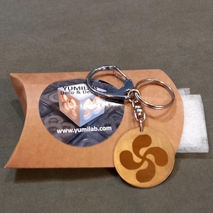 Peut inclure: Un porte-clés en bois avec un trèfle à quatre feuilles brun et un anneau de clé argenté. Le porte-clés est emballé dans une enveloppe en papier brun avec une étiquette qui indique "YUMILAB Deco & Design" et "www.yumilab.com".