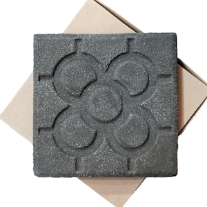 Può includere: Una piastrella quadrata nera con un design in rilievo di cinque cerchi sovrapposti. La piastrella ha una superficie ruvida e testurizzata.