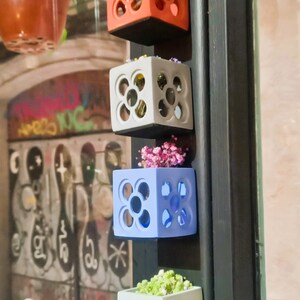 Peut inclure: Quatre pots muraux de différentes couleurs, chacun avec un motif géométrique et une petite plante. Les pots sont en céramique et ont un aspect moderne.