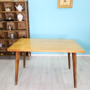 May include: A light wood table with a rectangular top and four legs. The table is on a white wood floor.