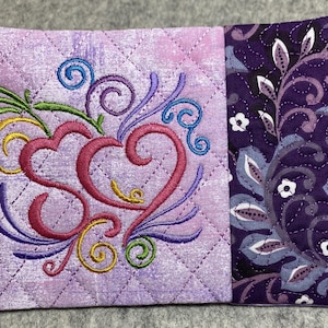 May include: A purple quilted pouch with a pink heart and floral embroidery design. The pouch is made of two different fabrics, one with a floral pattern and the other with a quilted design.