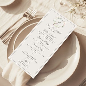 May include: A wedding menu card featuring a floral wreath design and the text "Mark & Jasmine" at the top. The menu includes "First Course", "Second Course", "Third Course", and "Dessert".