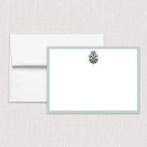May include: A stationery set featuring a white envelope and a matching card. The card has a light blue border and a floral design in the upper right corner. The floral design is blue and green.