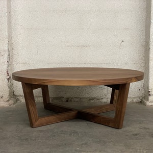 May include: A round, wooden coffee table with a dark brown finish. The table has a solid, circular top and a base with angled legs that intersect in an X-shape. The table is approximately 36 inches in diameter.