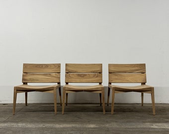 May include: Three wooden chairs with a simple design, featuring a curved seat and a slatted back. The chairs are made of natural wood and have a light brown finish.