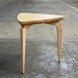 May include: A triangular wooden side table with three legs. The table is made of light wood and has a natural finish.