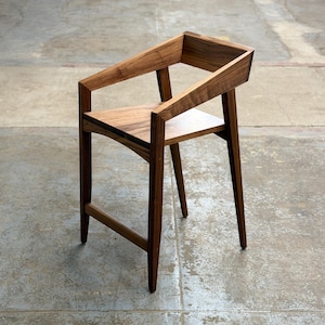 May include: A handcrafted wooden chair with a minimalist design. The chair features a dark brown finish, a seat, backrest, and armrests. The chair's dimensions are approximately 30 inches high, 18 inches wide, and 18 inches deep. The chair is made of solid wood.