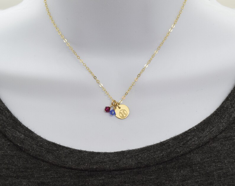 May include: A gold chain necklace with a small gold charm featuring a baseball design. The charm is accented with a red and blue crystal.