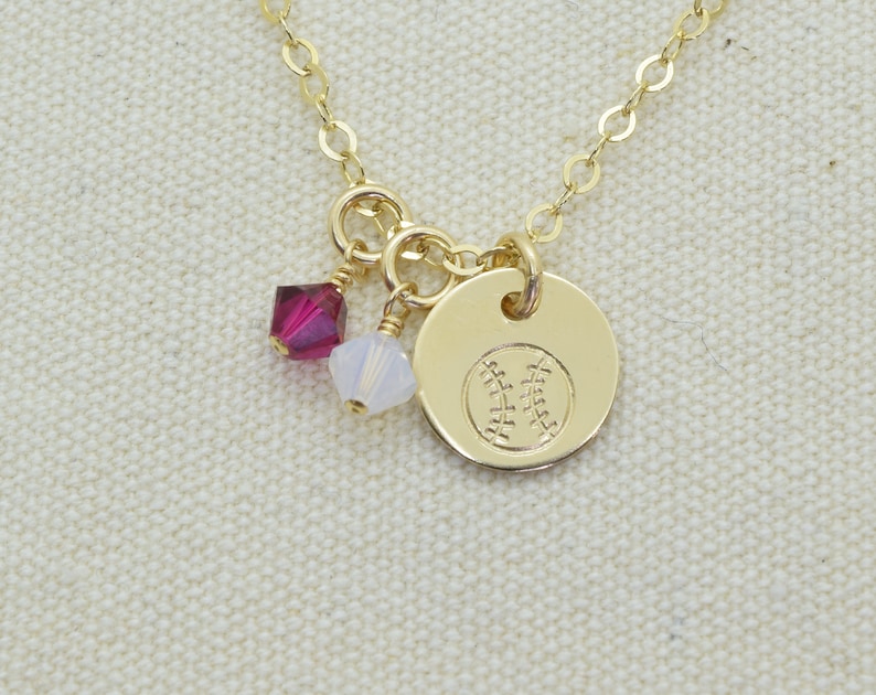 May include: Gold necklace with a baseball charm and two small crystal beads. The beads are red and white.