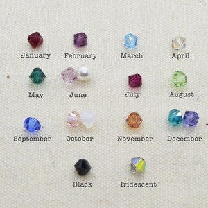 May include: A chart of crystal beads representing each month of the year. The beads are arranged in rows with the month name written below each bead. The beads are in various colors, including red, purple, blue, green, white, and black.