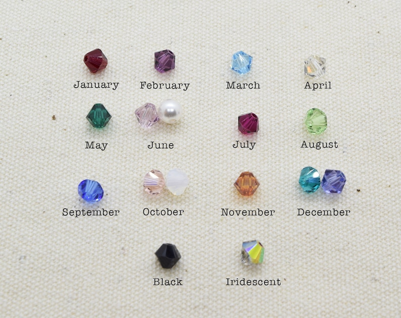 May include: A chart of crystal beads representing each month of the year. The beads are arranged in rows with the month name written below each bead. The beads are in various colors, including red, purple, blue, green, white, and black.