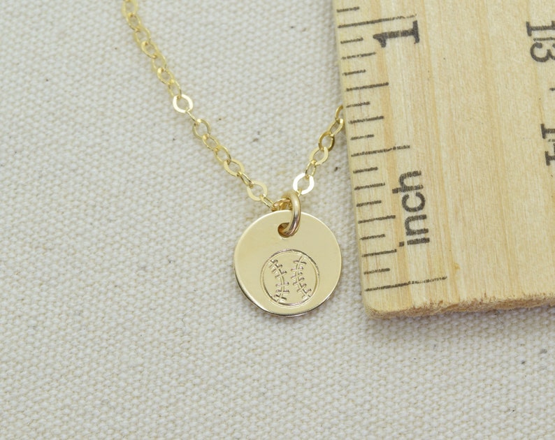 May include: A gold chain necklace with a small gold pendant featuring a baseball design. The pendant is about 1/2 inch in diameter.