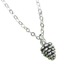 May include: A silver-colored necklace featuring a detailed pine cone pendant. The pendant is intricately designed with textured scales, and the chain is a simple, linked style. The necklace is displayed against a white background.