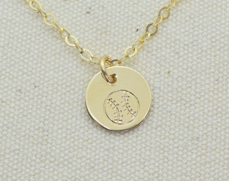 May include: A gold chain necklace with a small round pendant featuring a baseball design.