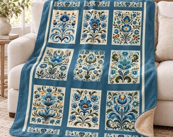 May include: A blue fleece throw blanket featuring a grid of rectangular panels, each decorated with intricate floral motifs in shades of blue, green, and cream. The blanket has a soft, textured cream-colored sherpa lining visible at the corner.