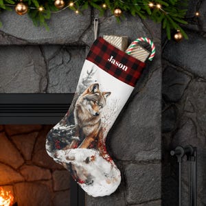 Puede incluir: Una media de Navidad personalizada con un puño de cuadros rojos y negros y una ilustración de un lobo. La media está llena de regalos y un bastón de caramelo. El nombre "Jason" está bordado en el puño.