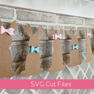May include: A brown paper bunny banner with pink and blue bows. The banner is hanging on a brick wall. The text "SVG Cut Files" is at the bottom of the image.