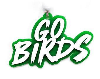 May include: Green and white acrylic ornament with a string for hanging. The ornament says "GO BIRDS" in white lettering.