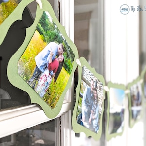 May include: A garland of framed photos, each in a light green decorative border, hangs in front of a window. The photos depict couples in outdoor settings. The garland is attached with small white clips.