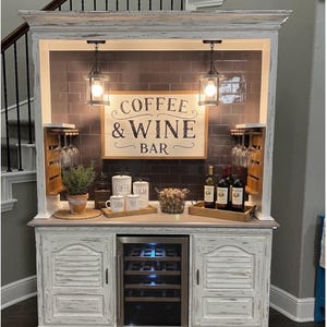May include: A white ceramic mug with a black handle and the text "But First, Coffee" in a black, handwritten-style font. The mug is on a white surface.