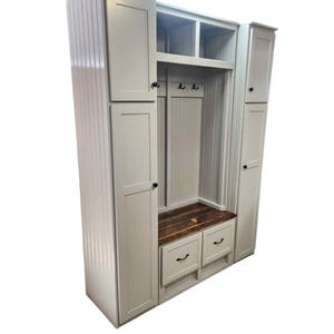 May include: A tall, light gray wooden entryway storage unit with multiple cabinets, drawers, and a bench. The unit has a vertical plank design on the sides and a dark wood-toned bench seat. Black knobs and hooks are visible.