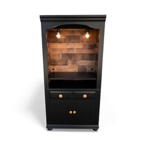 May include: A black cabinet with a wooden plank interior and two small shelves. The cabinet has two doors and two drawers with wooden knobs. Two light fixtures hang from the top of the cabinet.