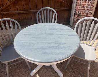 May include: A round, gray wooden table with a white base and four gray wooden chairs. The table and chairs are arranged in a circle.