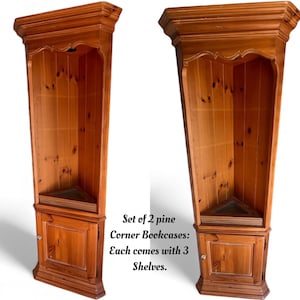 May include: Two pine corner bookcases with three shelves each. The bookcases are a light brown color and have a triangular shape. The text on the image says "Set of 2 pine Corner Bookcases: Each comes with 3 Shelves."