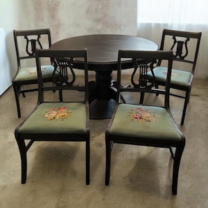 May include: A dark brown dining table with four matching chairs. The chairs have a lyre-shaped back and a green seat cushion with a floral design. The table is round and has a pedestal base.