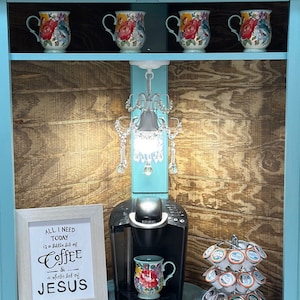 May include: A teal coffee station with a Keurig coffee maker, floral mugs, and a framed sign that reads "All I need today is a little bit of coffee & a whole lot of Jesus." A small chandelier hangs above the coffee maker.
