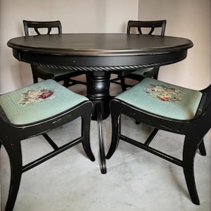 May include: A black round dining table with four matching chairs. The table has a decorative rope-like edge. The chairs have floral patterned seats in shades of blue, pink, and yellow. The furniture is set on a light-colored floor.