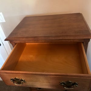 Puede incluir: C&oacute;moda de madera con un caj&oacute;n abierto. La c&oacute;moda es de color marr&oacute;n claro con tiradores dorados. El caj&oacute;n abierto revela el interior. La veta de la madera es visible.