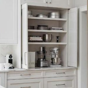 May include: White kitchen cabinets with a pull-down door revealing shelves stocked with kitchen appliances, cookware, and dishes.