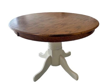 May include: A round wooden dining table with a white pedestal base. The table top is a dark wood with a natural grain pattern. The base has four legs that curve out from the pedestal.