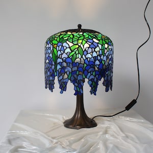 Könnte beinhalten: Eine Tischlampe aus Tiffany-Glas mit einem blauen und grünen Blumendesign. Die Lampe hat einen bronzenen Sockel und ein schwarzes Kabel.