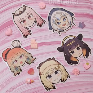 May include: Five colorful cartoon character stickers with different expressions. The stickers are on a pink and white marbled background. The characters are a pink haired girl with a crown, a white haired girl with a shark fin, a girl with orange hair and a feather, a girl with yellow hair and a hat, and a girl with black hair and a halo.
