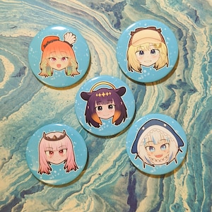 May include: Five round blue and white buttons with cartoon characters on them. The characters are all female and have different hair colors and styles. The buttons are about 2 inches in diameter.