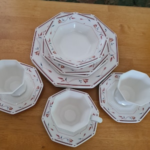 Puede incluir: Un juego de vajilla octogonal blanca con un diseño floral en rojo y azul. El juego incluye platos, cuencos y tazas de té con platillos. La vajilla está dispuesta sobre una superficie de madera.