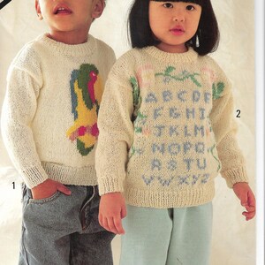 May include: Two children's sweaters. One is cream-colored with a colorful parrot design. The other is cream-colored with the alphabet in blue and green. The text "DOUBLE KNITTING" and size information are visible.