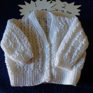 May include: White knitted baby cardigan with button fastenings. The cardigan is labelled "1 12-13 months" and "2 12-13 Kgs".